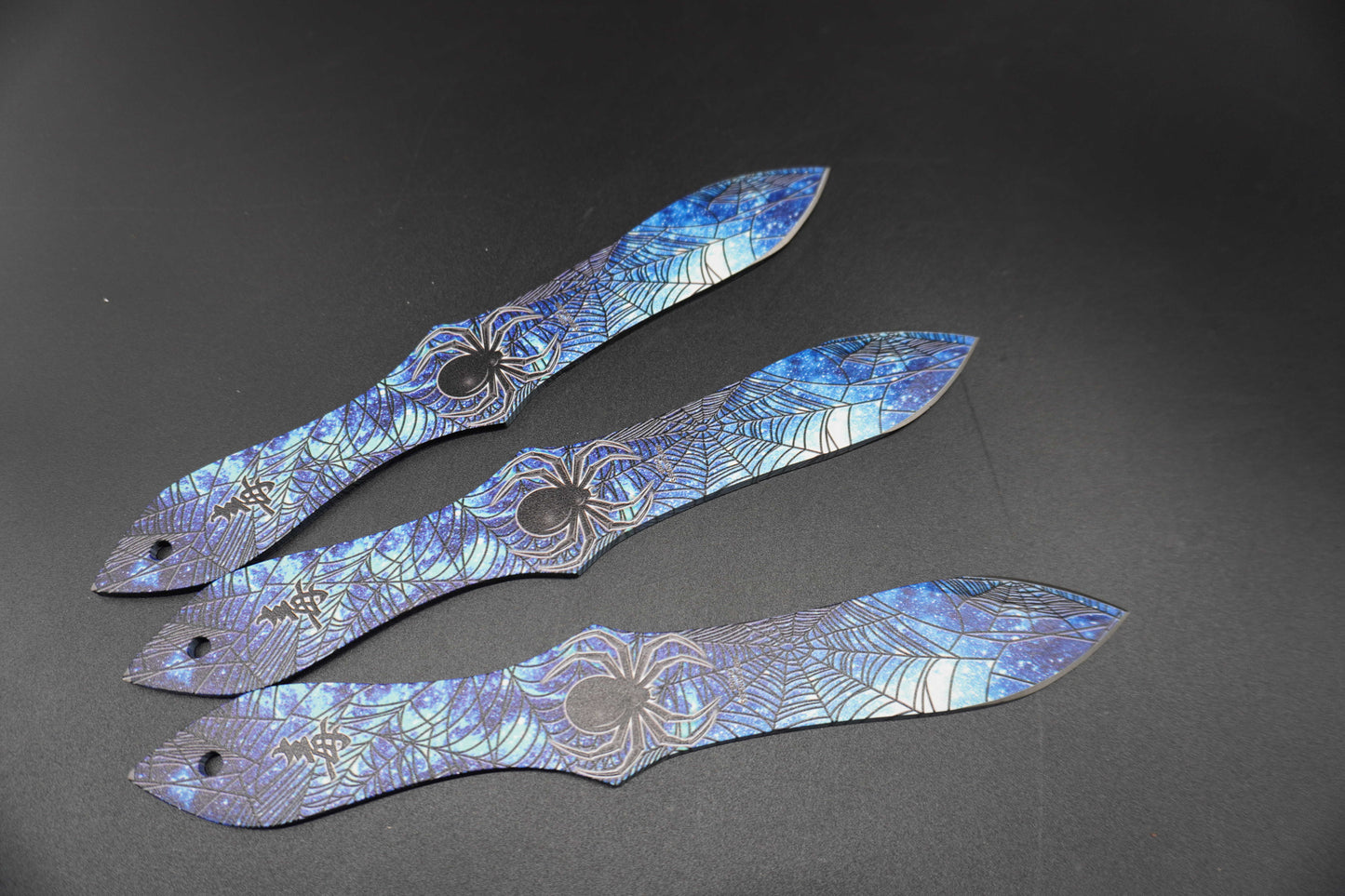 Three decorative blades with spider designs on a dark background