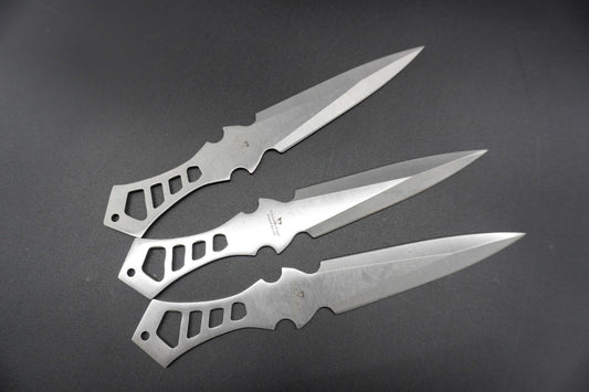 Three metallic throwing knives on a dark surface